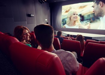 cinema, entertainment, communication and people concept - happy couple of friends watching movie and talking in theater from back